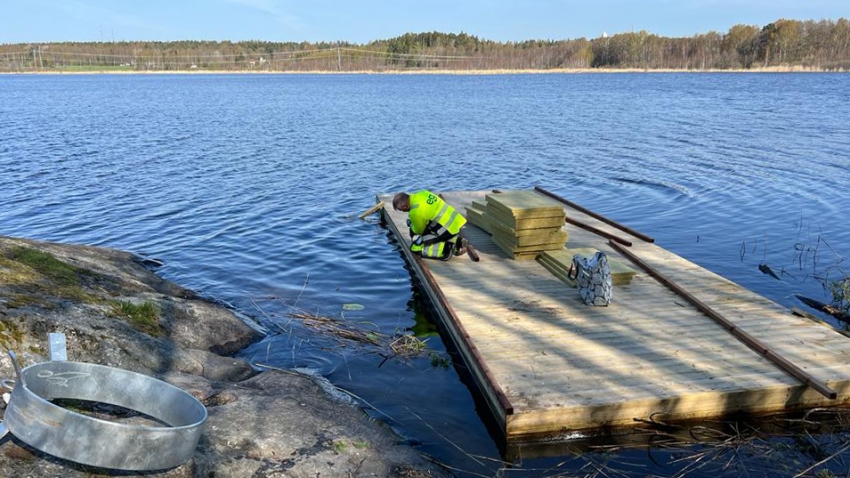 Lintusaareen, joka on puusta valmistettu lautta, asennetaan reunalistoja Lepinjärvellä Karjaalla. Asentaja Eg-Trading Oy.